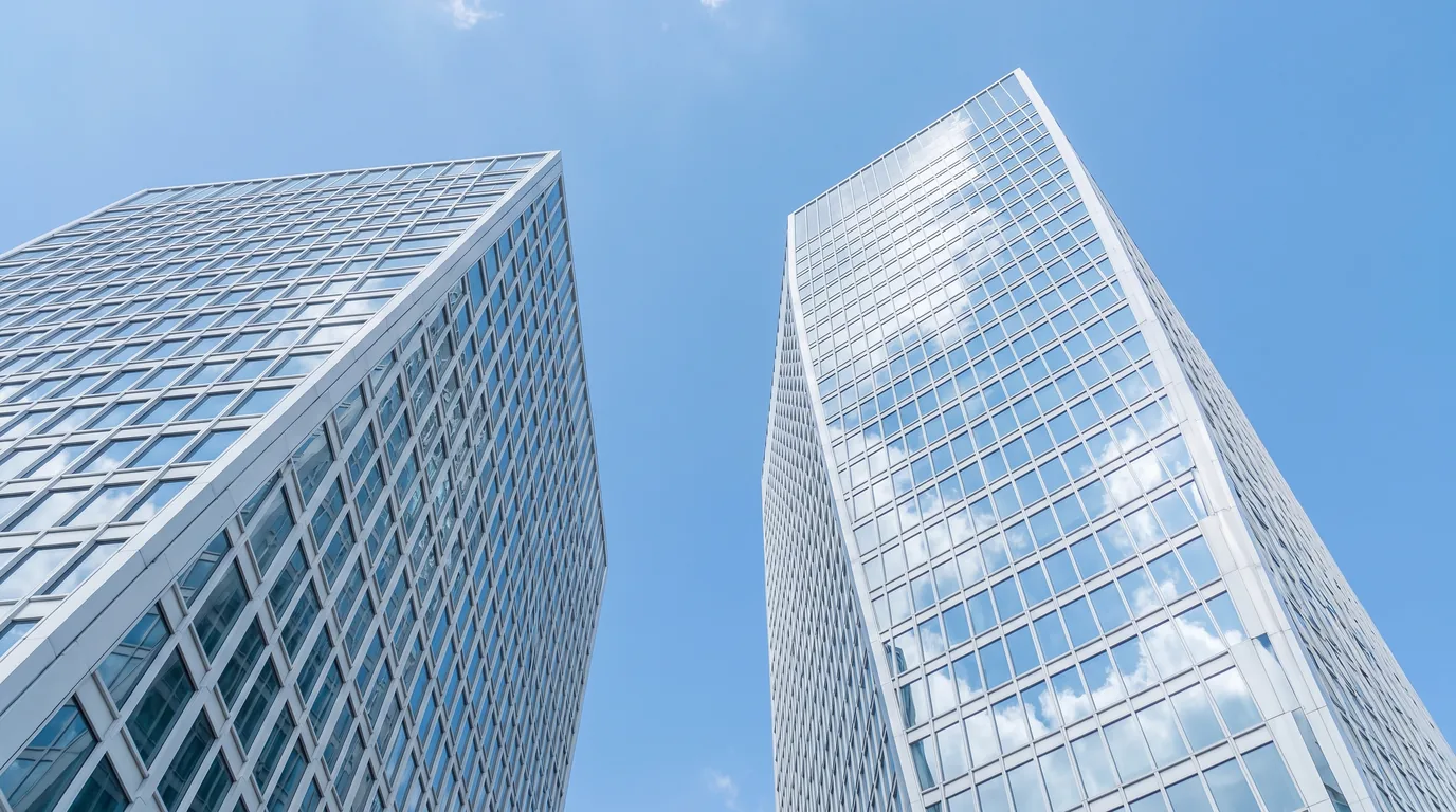 Zwei moderne Bürohochhäuser mit Glasfassade von unten fotografiert, dahinter blauer Himmel
