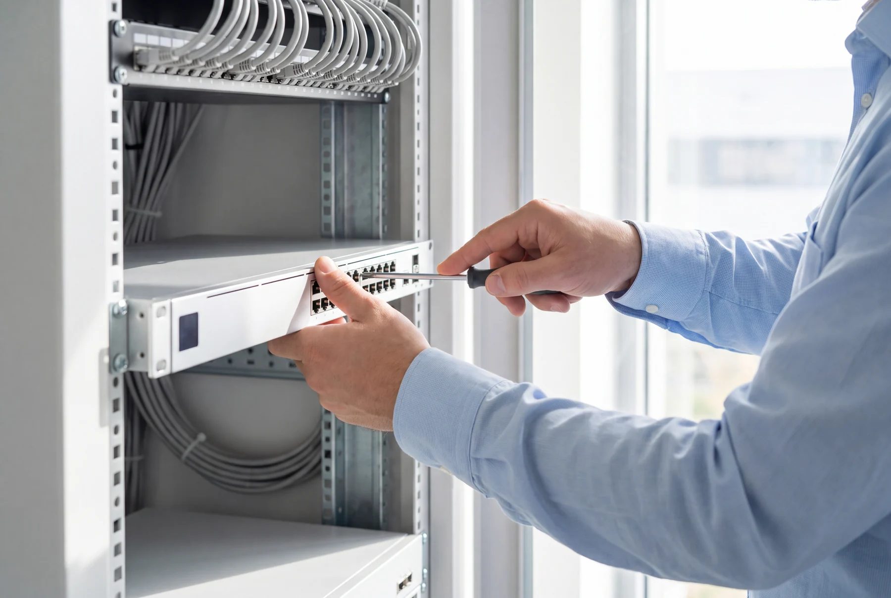 Hände montieren einen fabrikneuen Netzwerk-Switch mit einem Schraubendreher in einen Serverschrank