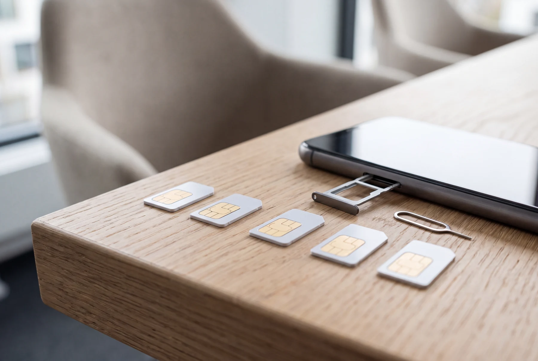 Fünf SIM-Karten nebeneinander auf einem Schreibtisch, daneben ein Smartphone mit herausgezogenem Kartenschacht